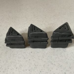 Three black plastic corner protectors arranged on a speckled surface.
