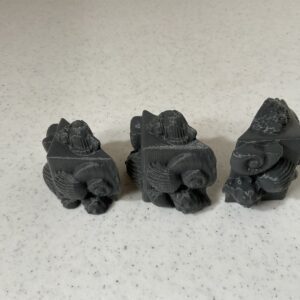 Three small, dark figurines arranged in a row on a light surface.