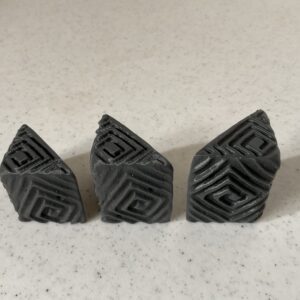 Three black geometric stone carvings on a speckled surface.
