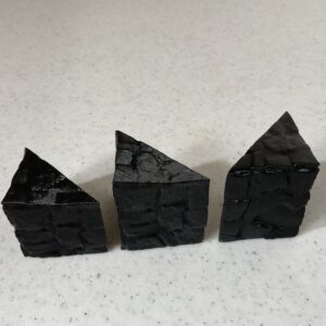 Three small, black, pyramid-like stone sculptures on a white surface.