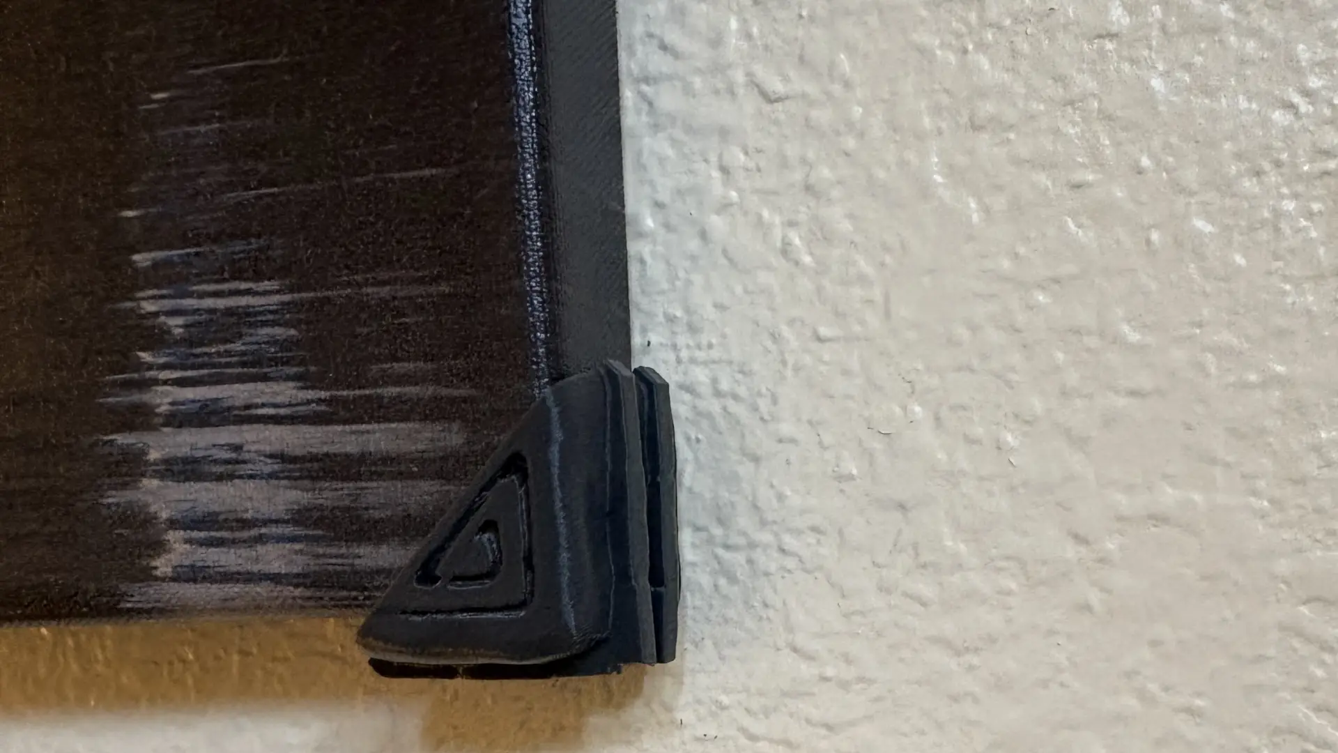 Close-up of a black corner protector on a picture frame against a textured wall.